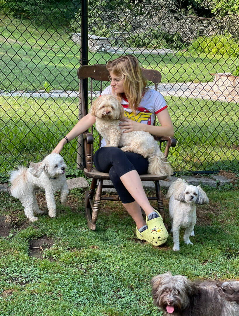 A woman sitting on a chair playing with three small dogs outdoors.